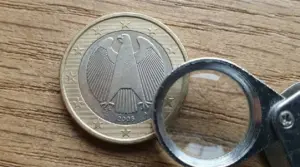 Moneta da 1 euro tedesca del 2008 esaminata con una lente d'ingrandimento su un tavolo in legno