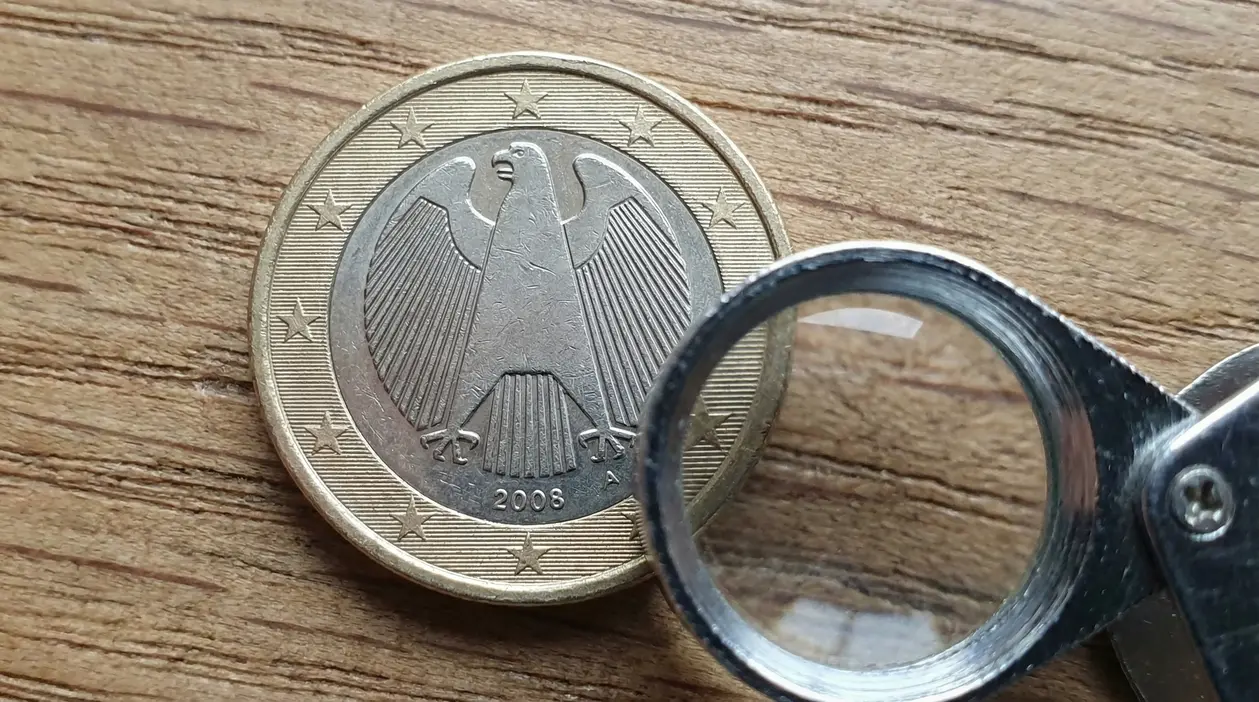Moneta da 1 euro tedesca del 2008 esaminata con una lente d'ingrandimento su un tavolo in legno