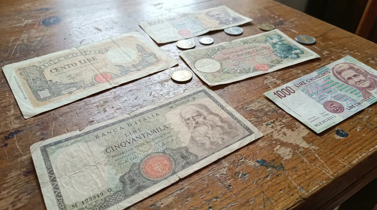 Vecchie banconote e monete italiane in lire sparse su un tavolo di legno