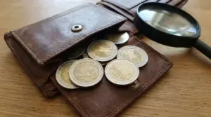 Monete da 2 euro sparse su un vecchio portafoglio accanto a una lente d'ingrandimento