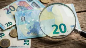 Banconote da 20 euro esaminate con lente d'ingrandimento su tavolo in legno