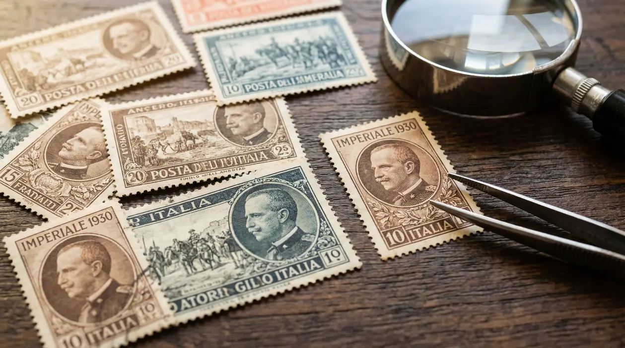 Francobolli della serie Imperiale 1930 su tavolo in legno con lente d'ingrandimento e pinzette