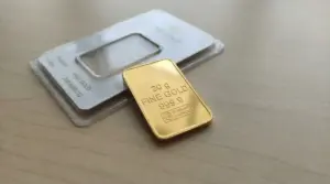 Lingotto d'oro da 20 grammi su una superficie chiara accanto alla sua confezione.