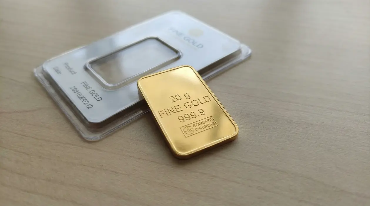 Lingotto d'oro da 20 grammi su una superficie chiara accanto alla sua confezione.
