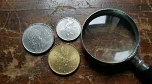 Tre monete italiane del 1970 con una lente d'ingrandimento su un tavolo di legno