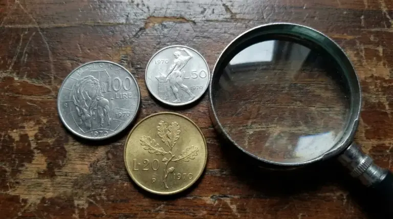Tre monete italiane del 1970 con una lente d'ingrandimento su un tavolo di legno