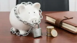 Salvadanaio bianco con catena e lucchetto accanto a monete e taccuino su scrivania