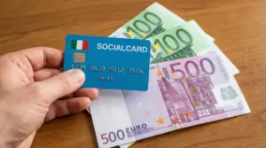 Mano che tiene una social card italiana sopra banconote in euro