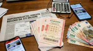 Biglietti del Superenalotto, banconote in euro, giornale e smartphone su un tavolo.