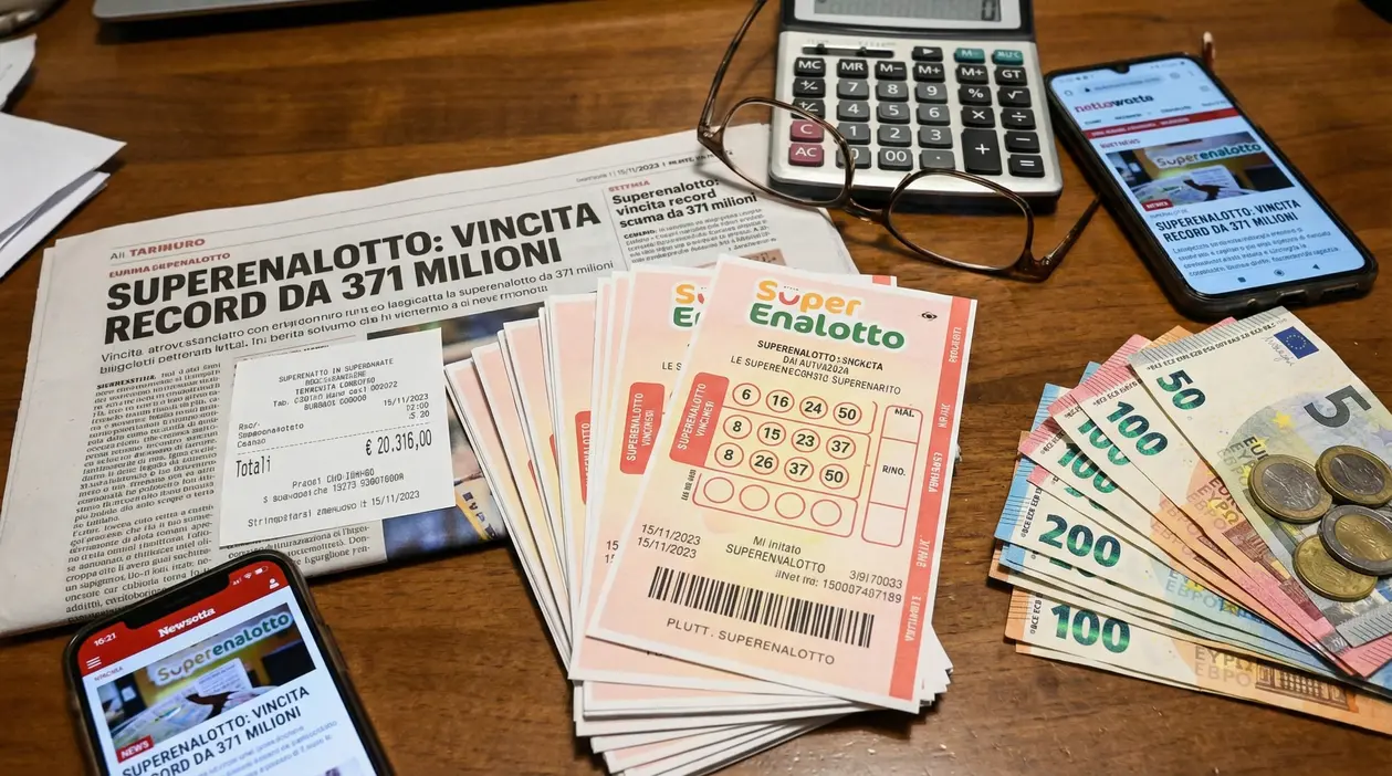 Biglietti del Superenalotto, banconote in euro, giornale e smartphone su un tavolo.