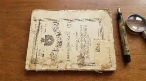 Vecchio libretto postale consunto accanto a una penna stilografica e a una lente d’ingrandimento su un tavolo in legno